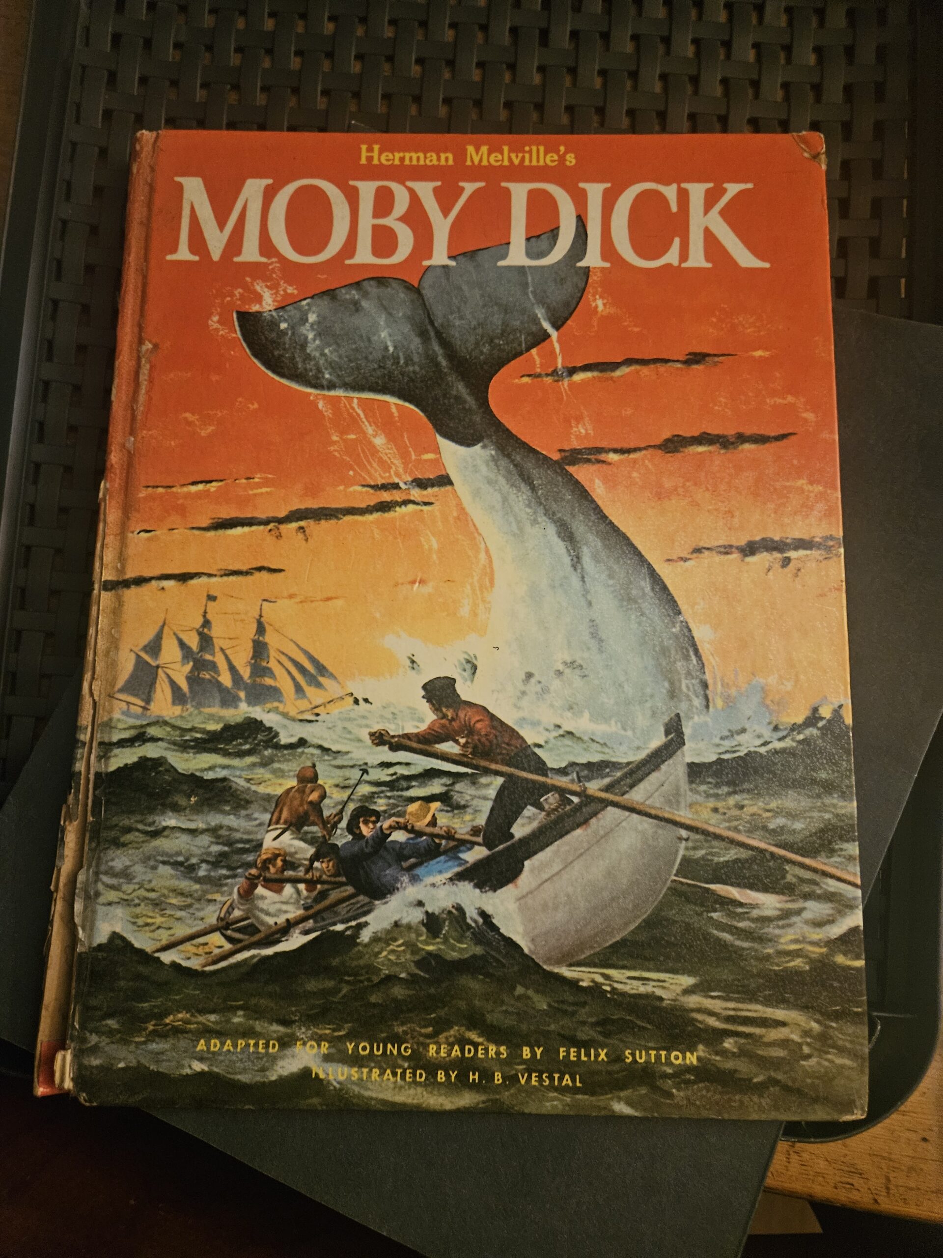 A vintage copy of Moby Dick with an orange background and illustration of a whale's tail coming out of the sea.